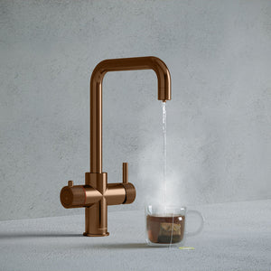 a copper square-shaped boiling water tap dispensing hot water to a cup of tea