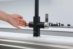 Person turning a black kitchen faucet with a silver handle on a white countertop.