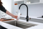 Person washing dishes in a modern kitchen with a black faucet.