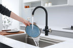 Person washing a blue plate under a black faucet in a modern kitchen.