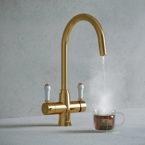 a traditional brushed gold swan neck kitchen hot tap with white handle