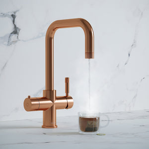 a rose gold square-shaped boiling water tap dispensing hot water to a cup of tea