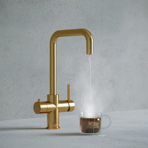 a brushed gold square-shaped boiling water tap dispensing hot water to a cup of tea