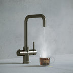a gunmetal grey square-shaped boiling water tap dispensing hot water to a cup of tea