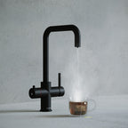a matt black square-shaped boiling water tap dispensing hot water to a cup of tea