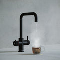 a matt black square-shaped boiling water tap dispensing hot water to a cup of tea
