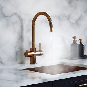 a brushed copper swan neck boiling water tap on a white kitchen countertop